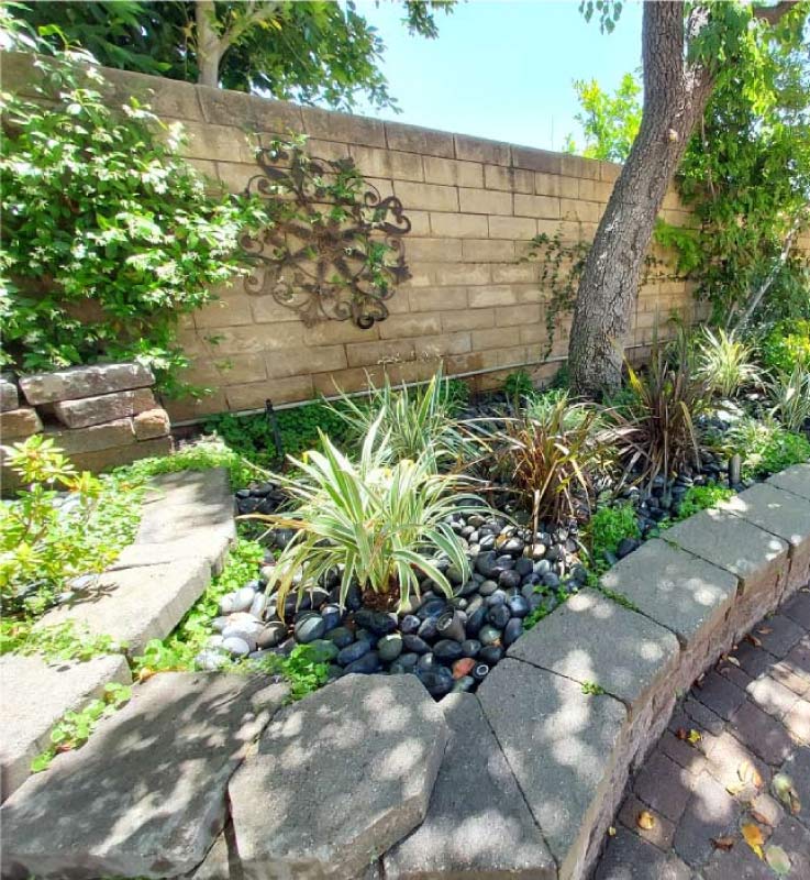  Upscale backyard landscaping in Manhattan Beach featuring a curved stone garden wall, decorative wall art, and a mix of green and purple ornamental plants.