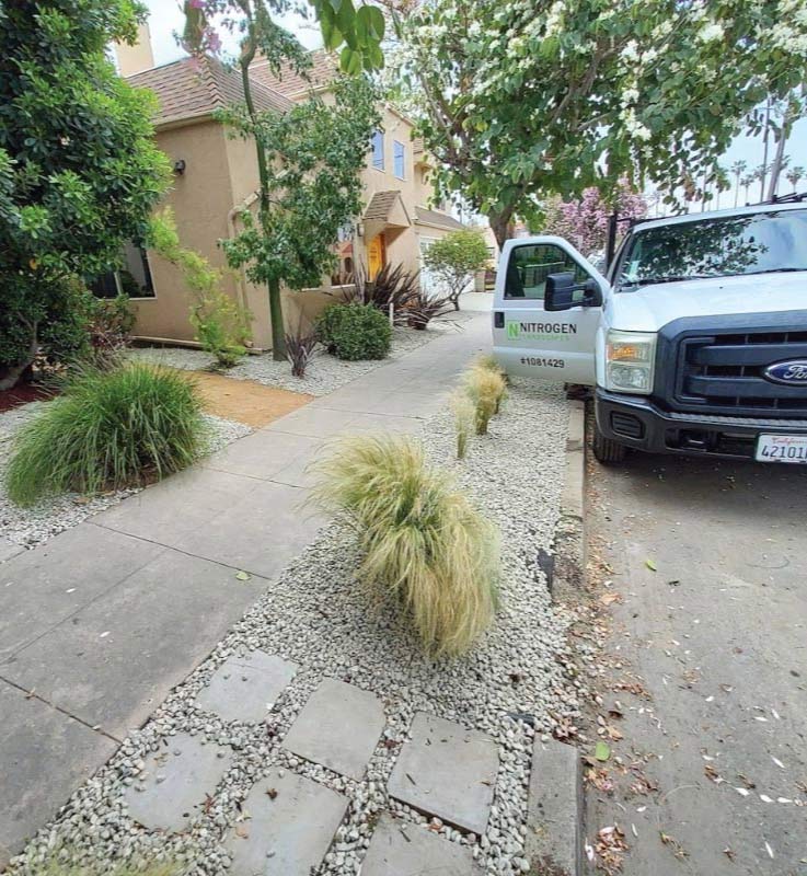 Drought-tolerant front yard landscaping in Los Angeles featuring a stamped concrete walkway, river rock garden bed, and succulent fire stick plants.