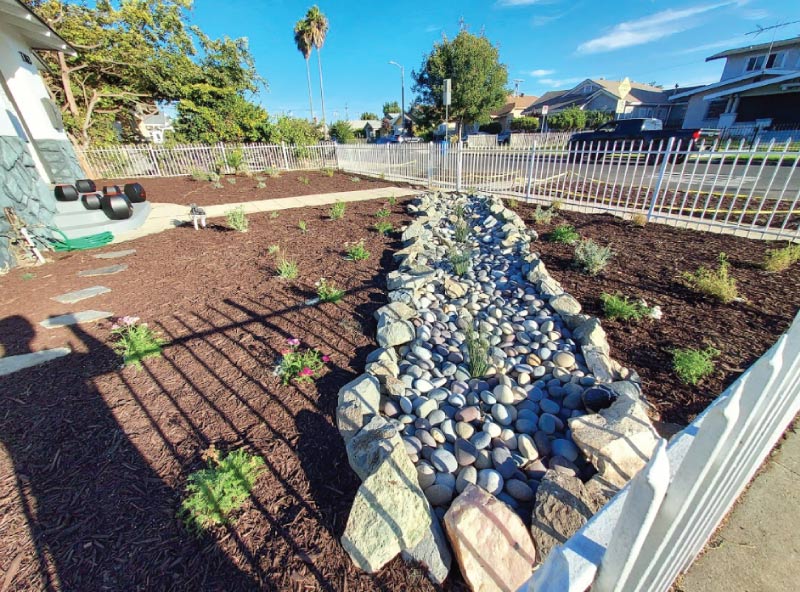 Sustainable dry creek bed installation featuring natural river rocks and wood mulch for effective stormwater management and drainage in a residential yard.