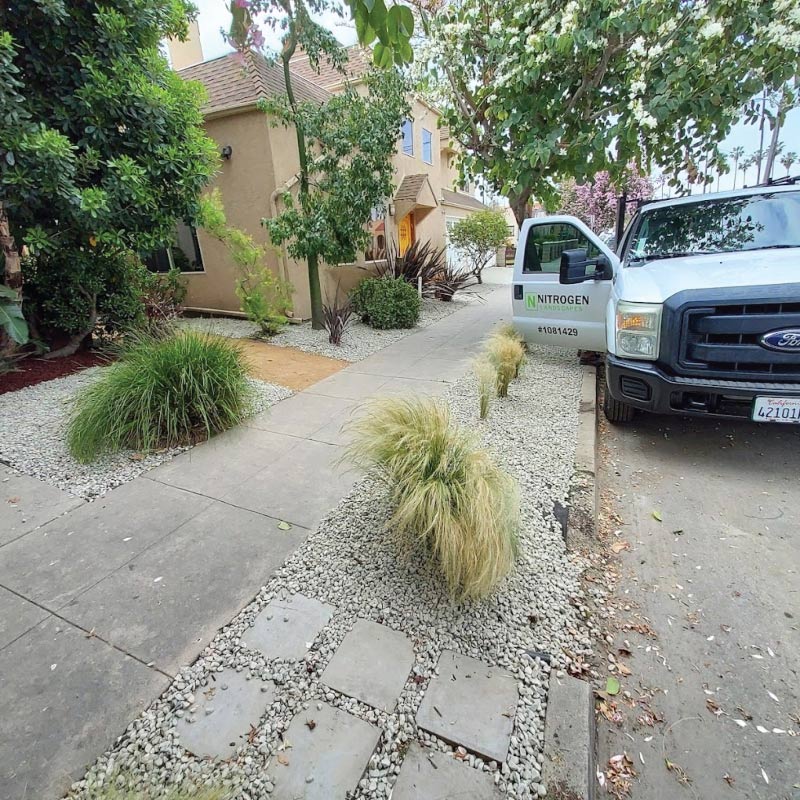 Nitrogen Landscapes service truck parked in front of a completed drought-friendly landscape project featuring decorative gravel and native grasses.